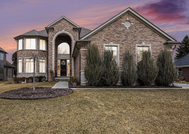 view of front of house featuring brick siding and a lawn