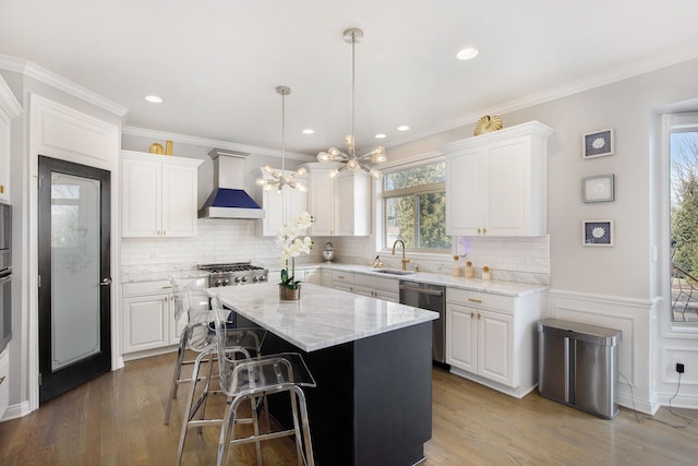 kitchen featuring wall chimney exhaust hood, appliances with stainless steel finishes, a sink, and white cabinetry