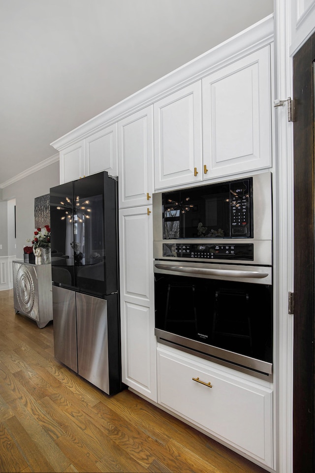 kitchen with white cabinetry, stainless steel appliances, wood finished floors, and ornamental molding