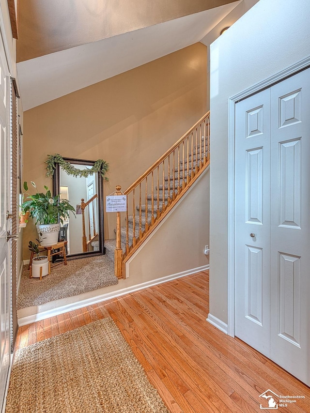 foyer entrance with stairs, lofted ceiling, baseboards, and wood finished floors