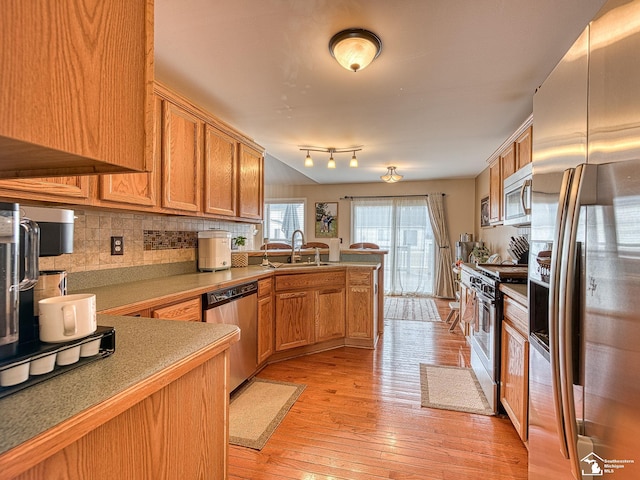 kitchen featuring light wood finished floors, stainless steel appliances, decorative backsplash, a sink, and a peninsula