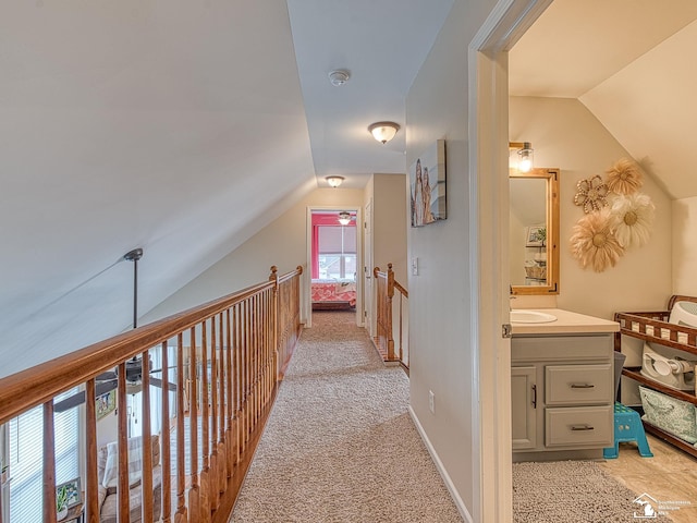 corridor featuring light carpet, baseboards, vaulted ceiling, and a sink