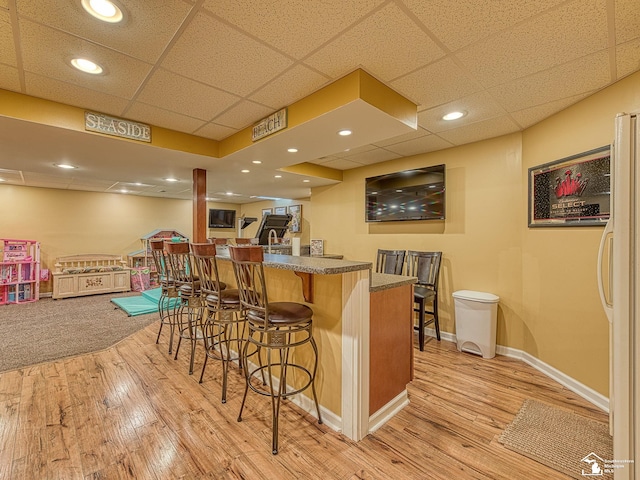 bar featuring freestanding refrigerator, baseboards, a bar, and light wood finished floors