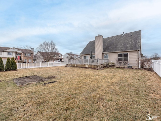 back of property with a fenced backyard, a chimney, a residential view, a yard, and a wooden deck