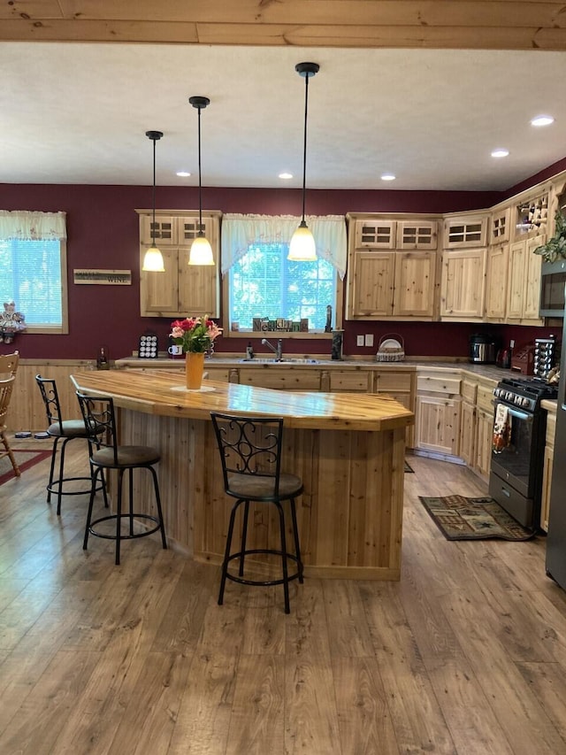 kitchen with gas stove, a kitchen island, a sink, wood finished floors, and butcher block countertops