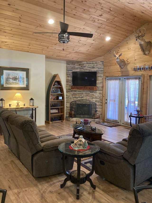 living room featuring a ceiling fan, vaulted ceiling, a stone fireplace, wood finished floors, and wooden ceiling