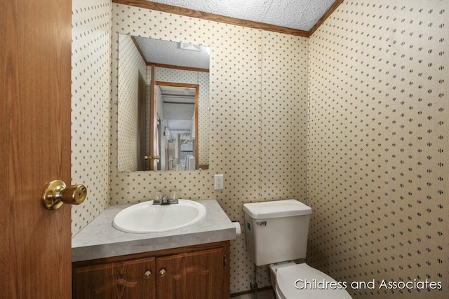 half bathroom with a textured ceiling, toilet, crown molding, vanity, and wallpapered walls