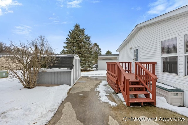 snowy yard featuring an outdoor structure, a wooden deck, and a shed