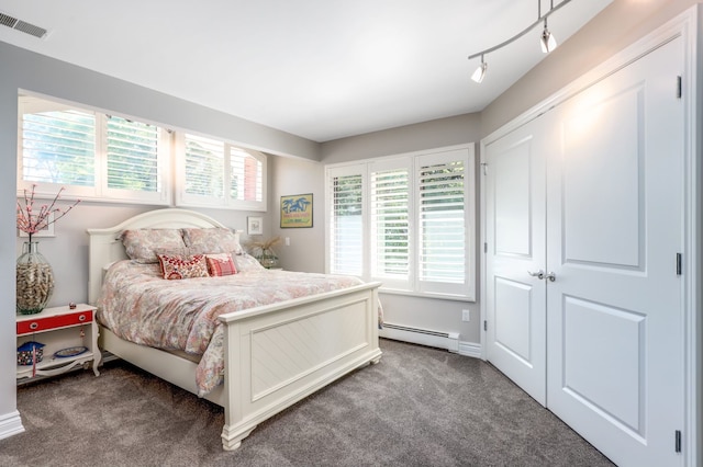 carpeted bedroom with visible vents, multiple windows, baseboard heating, and track lighting