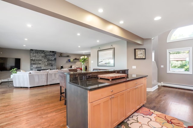 kitchen with a baseboard heating unit, light wood-type flooring, recessed lighting, a fireplace, and a kitchen breakfast bar