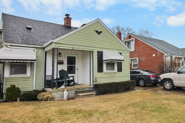 view of front of property with a chimney, a front lawn, a porch, and roof with shingles