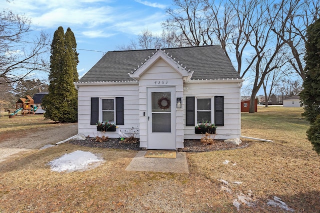 bungalow-style home with a shingled roof, a front lawn, and a playground