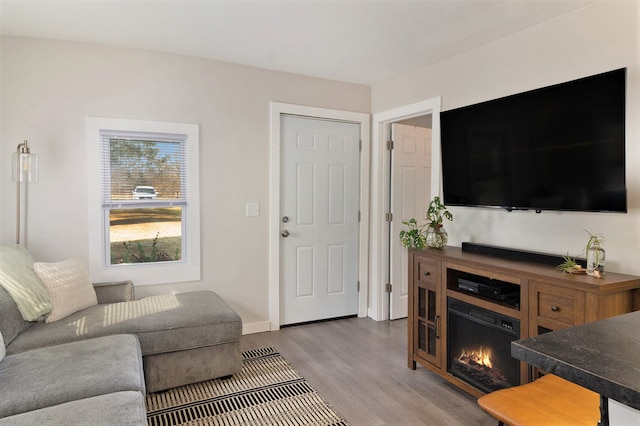 living area featuring a lit fireplace, light wood finished floors, and baseboards