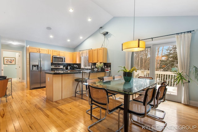 kitchen featuring stainless steel appliances, dark countertops, light brown cabinetry, light wood-style floors, and a peninsula