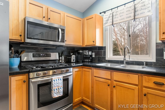 kitchen featuring appliances with stainless steel finishes, dark countertops, a sink, and decorative backsplash