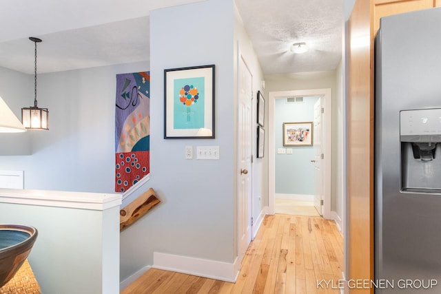 hallway with light wood finished floors, baseboards, visible vents, and a textured ceiling