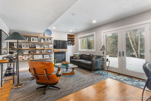 living room with a textured ceiling, a glass covered fireplace, wood finished floors, and french doors