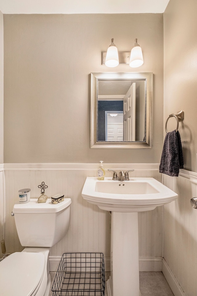 half bath with a wainscoted wall, a sink, and toilet