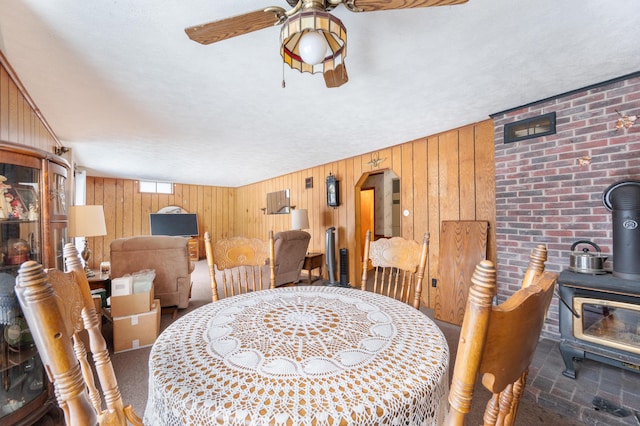 dining space with wooden walls, a wood stove, and a ceiling fan