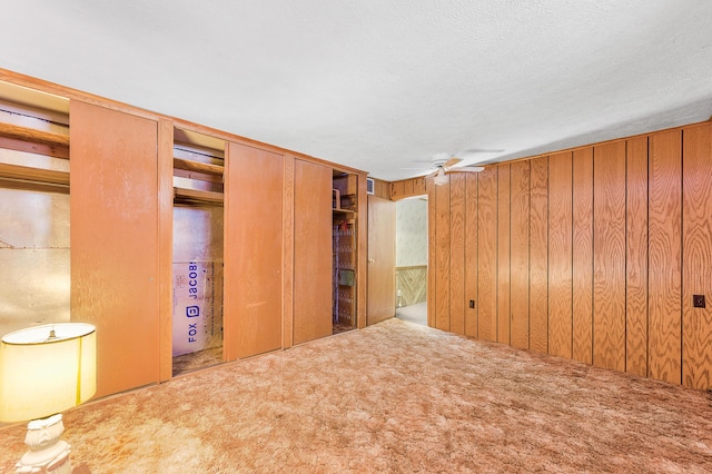 interior space featuring carpet floors, wooden walls, and a ceiling fan