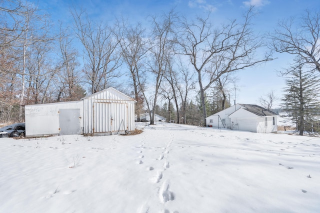 snowy yard featuring an outbuilding, a storage unit, and a garage