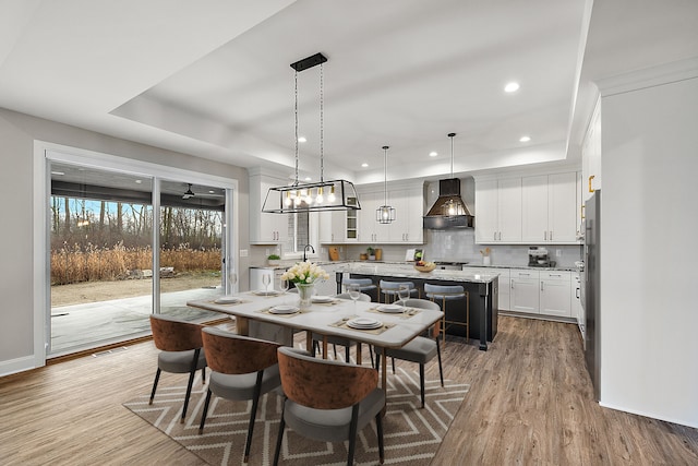 dining area with baseboards, a tray ceiling, wood finished floors, and recessed lighting