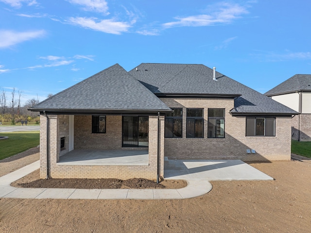 rear view of house with a patio area, a shingled roof, and brick siding