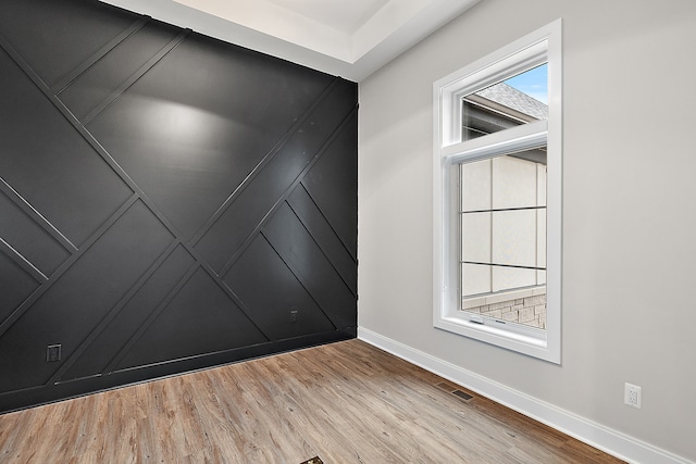 spare room featuring visible vents, a decorative wall, baseboards, and wood finished floors