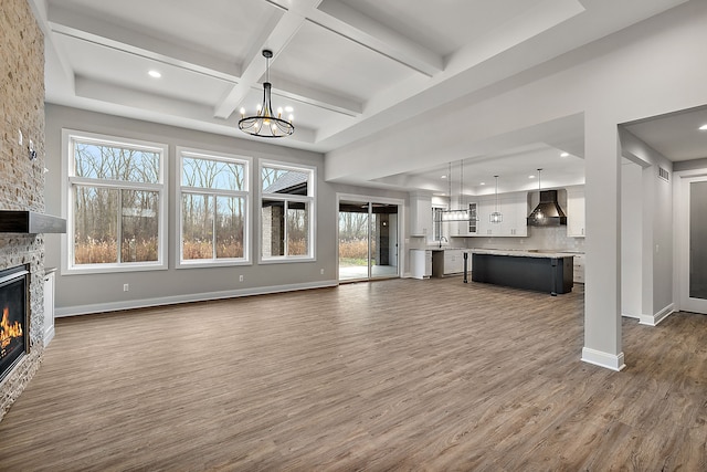 unfurnished living room with dark wood finished floors, a notable chandelier, a stone fireplace, and baseboards