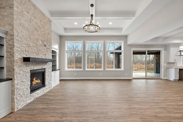 unfurnished living room with baseboards, a fireplace, a chandelier, and wood finished floors