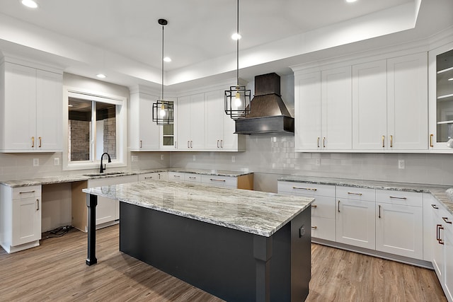 kitchen featuring light wood finished floors, custom range hood, glass insert cabinets, white cabinetry, and a sink