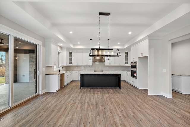 kitchen with glass insert cabinets, a center island, a sink, light wood-type flooring, and backsplash