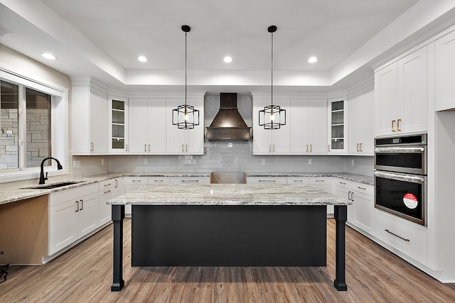 kitchen featuring stainless steel double oven, a sink, wood finished floors, premium range hood, and a kitchen bar