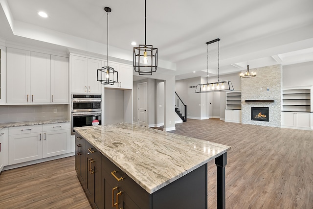 kitchen featuring decorative backsplash, white cabinets, wood finished floors, double oven, and a fireplace