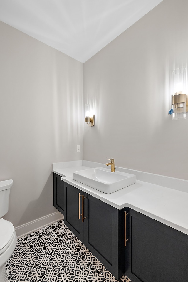 half bathroom featuring toilet, tile patterned flooring, baseboards, and vanity