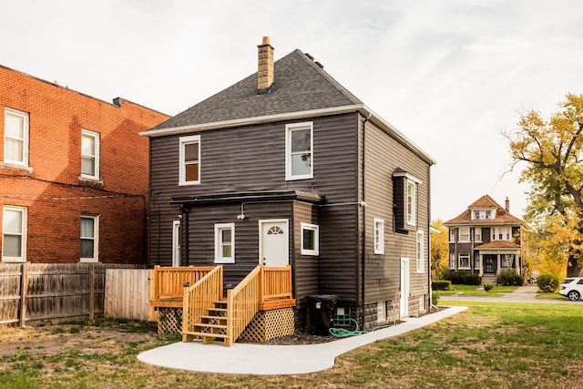 rear view of property featuring a shingled roof, a chimney, fence, and a lawn