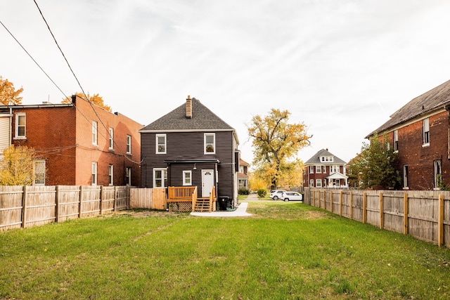 back of property featuring a deck, a lawn, a chimney, and a fenced backyard