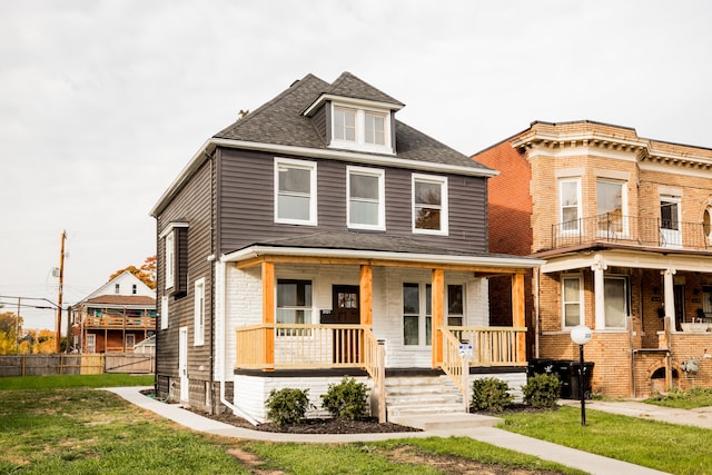 american foursquare style home featuring a shingled roof, covered porch, and a front lawn