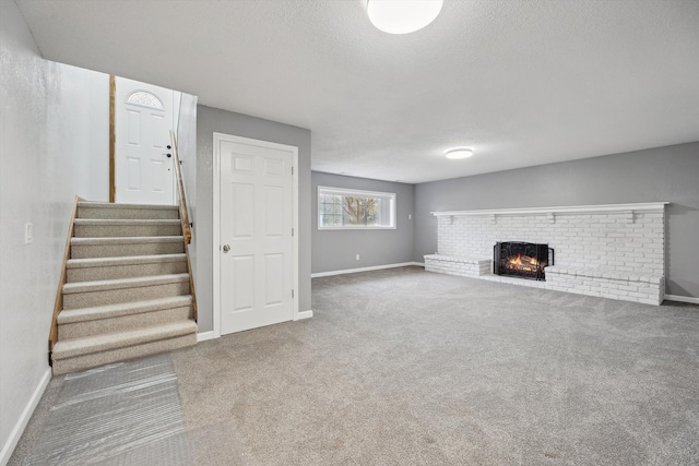 unfurnished living room featuring a brick fireplace, baseboards, stairs, carpet floors, and a textured ceiling