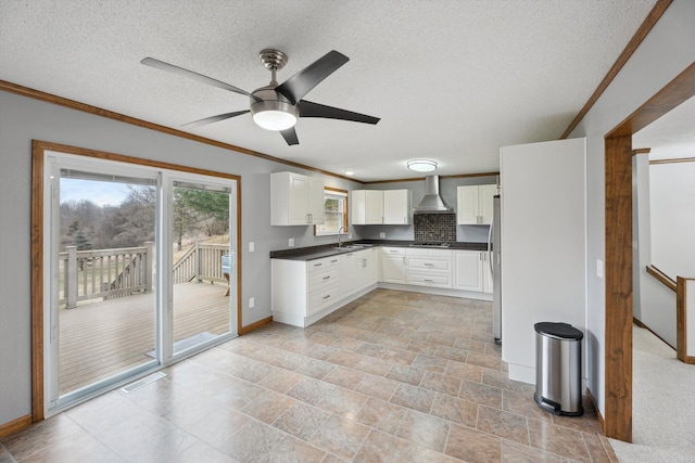 kitchen with dark countertops, ornamental molding, white cabinets, wall chimney exhaust hood, and a sink