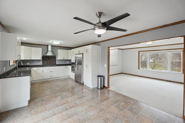 kitchen with ornamental molding, a sink, stainless steel refrigerator with ice dispenser, dark countertops, and wall chimney exhaust hood