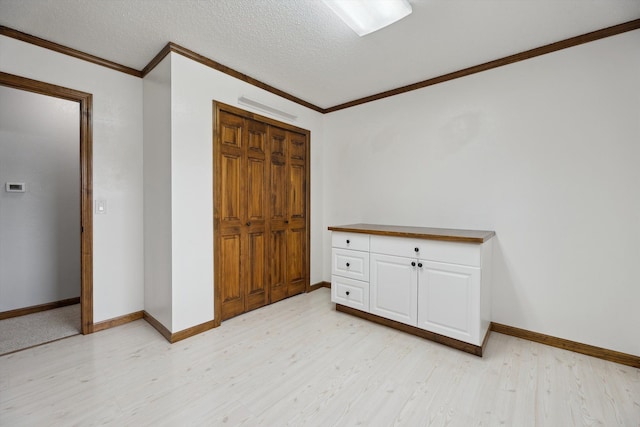 unfurnished bedroom featuring baseboards, light wood-style flooring, ornamental molding, a closet, and a textured ceiling