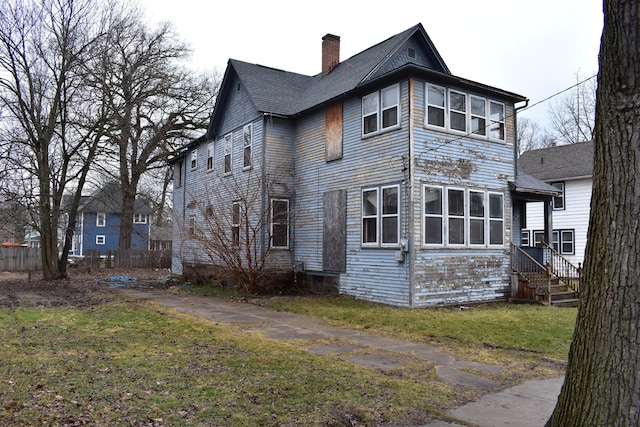 exterior space with a shingled roof, a chimney, fence, and a front yard