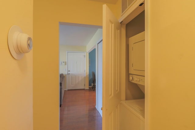 corridor with stacked washer / drying machine and dark wood finished floors