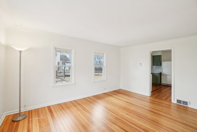 empty room with light wood-style flooring, visible vents, and baseboards