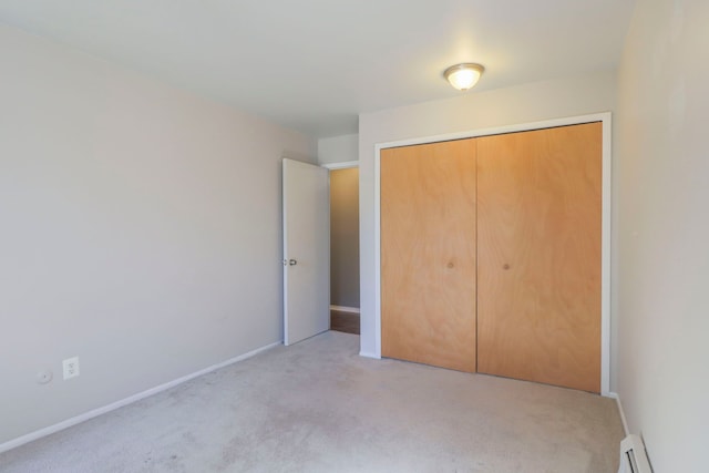 unfurnished bedroom with a closet, baseboards, light colored carpet, and a baseboard heating unit