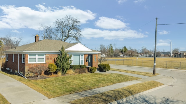 view of front facade with a front yard, a chimney, fence, and brick siding