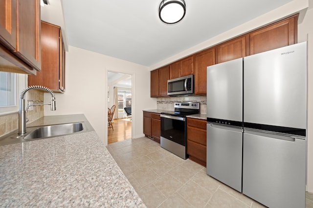 kitchen featuring brown cabinetry, decorative backsplash, stainless steel appliances, light countertops, and a sink