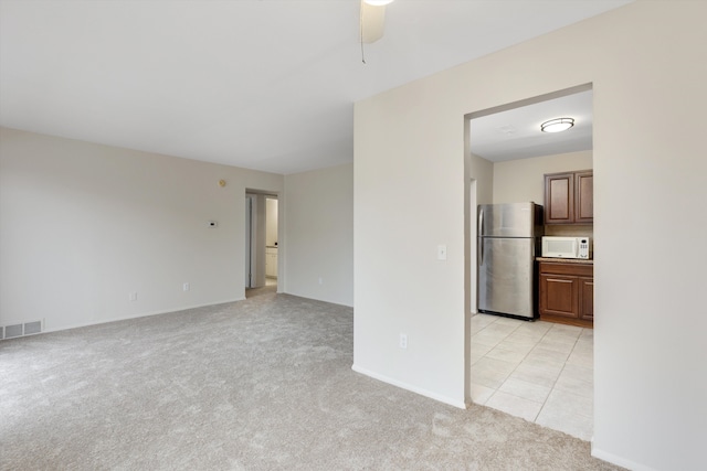 empty room featuring a ceiling fan, visible vents, light carpet, and baseboards