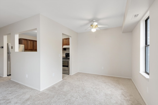 spare room featuring light colored carpet, ceiling fan, visible vents, and baseboards